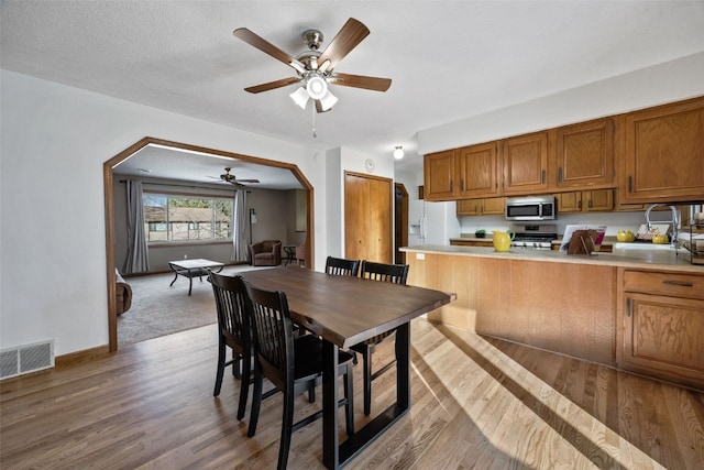 dining space featuring visible vents, baseboards, light wood-style flooring, arched walkways, and a ceiling fan