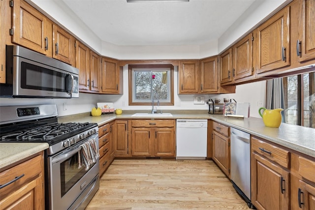 kitchen featuring a sink, stainless steel appliances, light countertops, light wood-style floors, and brown cabinets