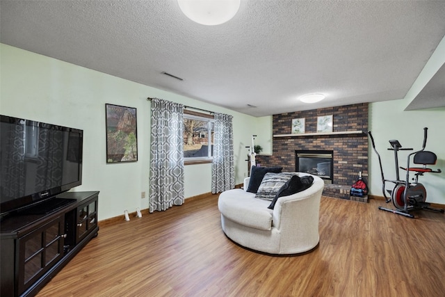 living area featuring visible vents, a textured ceiling, a brick fireplace, and wood finished floors