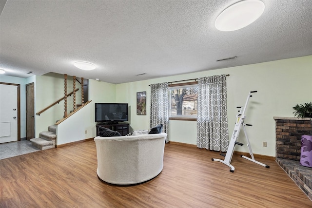 living room with a textured ceiling, stairs, baseboards, and wood finished floors