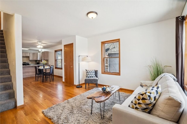 living room with baseboards, stairs, light wood-style floors, and a ceiling fan