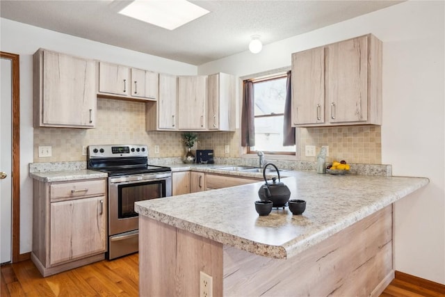 kitchen with a sink, a peninsula, electric range, and light brown cabinetry