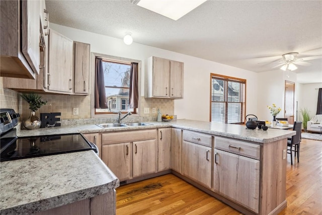 kitchen featuring a healthy amount of sunlight, light brown cabinetry, a peninsula, stainless steel range with electric cooktop, and a sink