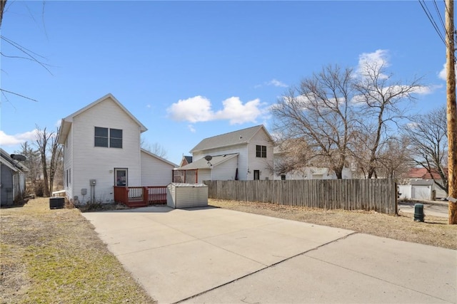 back of property with central AC, concrete driveway, and fence