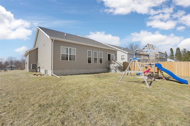 rear view of house with a playground, a yard, and fence