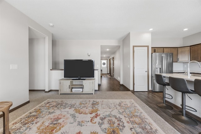 kitchen featuring baseboards, stainless steel fridge with ice dispenser, light countertops, a kitchen breakfast bar, and dark wood-style flooring