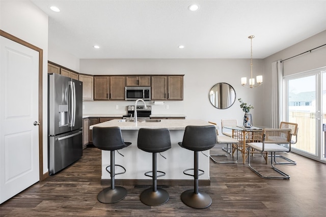 kitchen with dark wood-style floors, a kitchen island with sink, stainless steel appliances, hanging light fixtures, and a kitchen breakfast bar