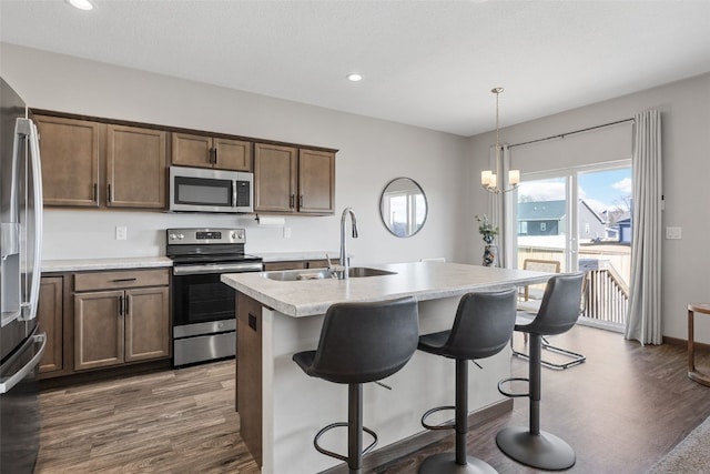 kitchen featuring an island with sink, a sink, wood finished floors, stainless steel appliances, and light countertops