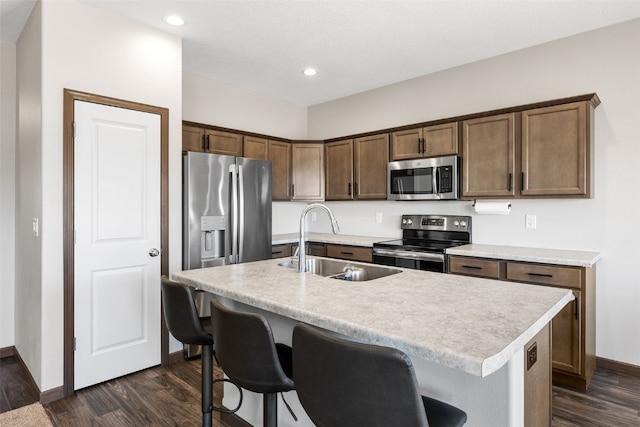 kitchen featuring dark wood finished floors, a kitchen island with sink, a sink, stainless steel appliances, and light countertops