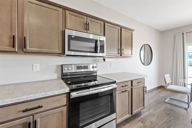 kitchen featuring light countertops, wood finished floors, baseboards, and appliances with stainless steel finishes