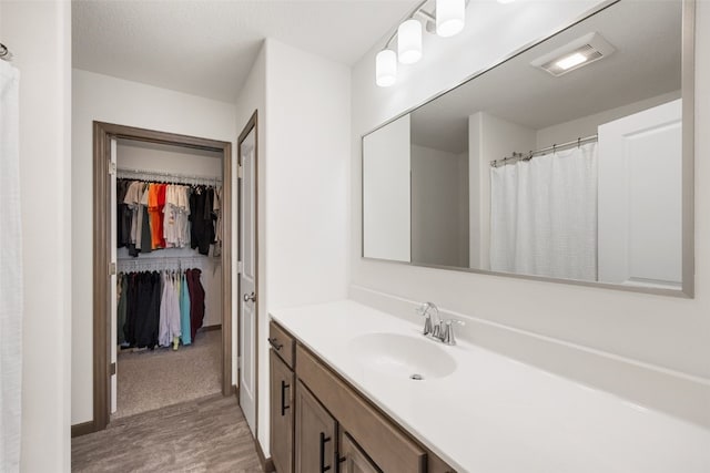 full bath featuring visible vents, a walk in closet, wood finished floors, baseboards, and vanity