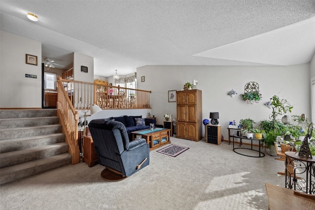 living area featuring stairway, ceiling fan with notable chandelier, carpet floors, and a textured ceiling