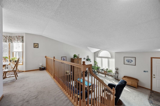 hall with an upstairs landing, carpet floors, baseboards, and vaulted ceiling