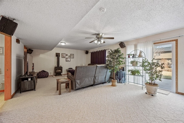 carpeted living room with baseboards, a textured ceiling, a wood stove, and a ceiling fan