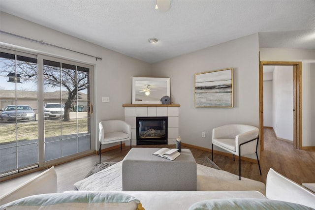 living area featuring a ceiling fan, wood finished floors, a tiled fireplace, and vaulted ceiling