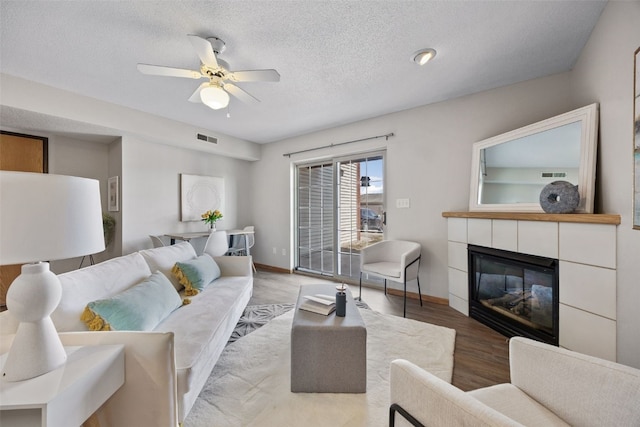 living area featuring wood finished floors, visible vents, ceiling fan, a textured ceiling, and a tiled fireplace