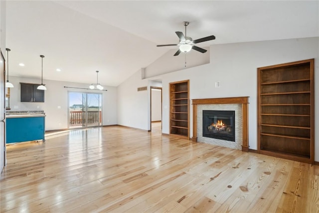 unfurnished living room with visible vents, ceiling fan, built in features, a tile fireplace, and light wood-style floors