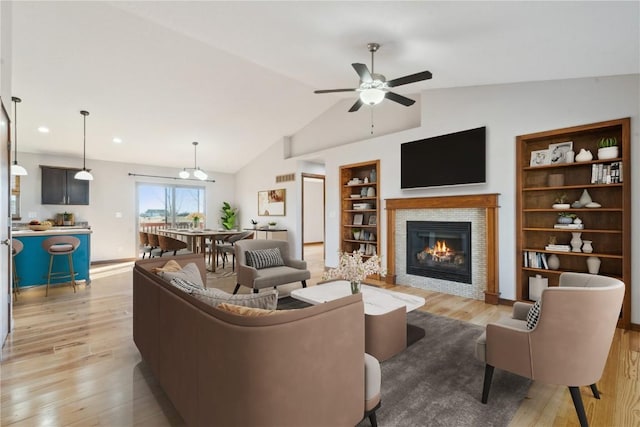 living area with light wood-type flooring, built in shelves, a tiled fireplace, lofted ceiling, and ceiling fan