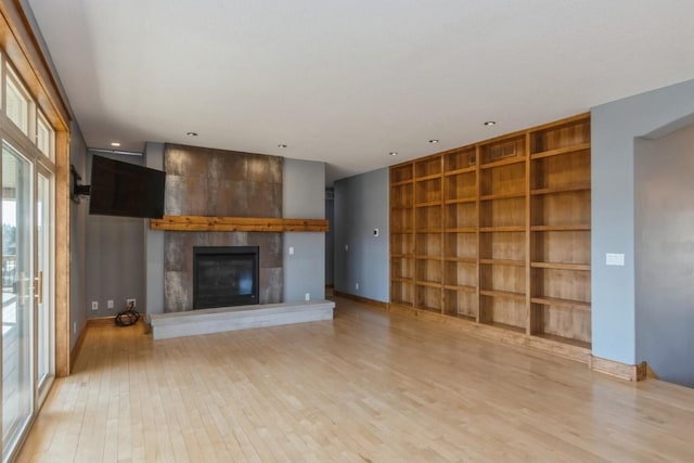 unfurnished living room with built in shelves, a fireplace, and light wood finished floors