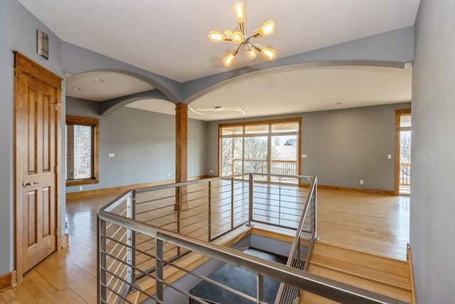 stairway with baseboards, decorative columns, wood finished floors, arched walkways, and a notable chandelier