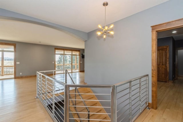 hall with wood finished floors, baseboards, arched walkways, a notable chandelier, and an upstairs landing