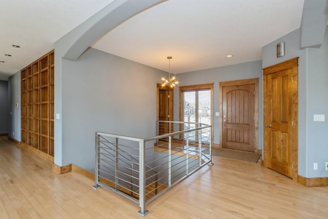 foyer entrance with wood finished floors, baseboards, recessed lighting, arched walkways, and a notable chandelier