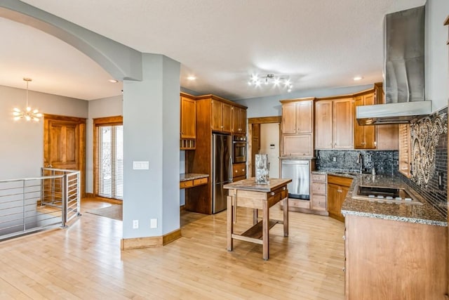 kitchen featuring backsplash, appliances with stainless steel finishes, island exhaust hood, light wood-style floors, and arched walkways