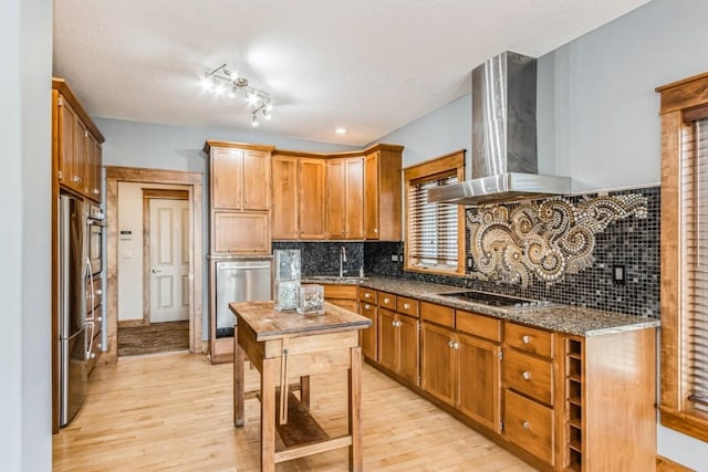 kitchen with wall chimney exhaust hood, light wood-style floors, appliances with stainless steel finishes, and a sink