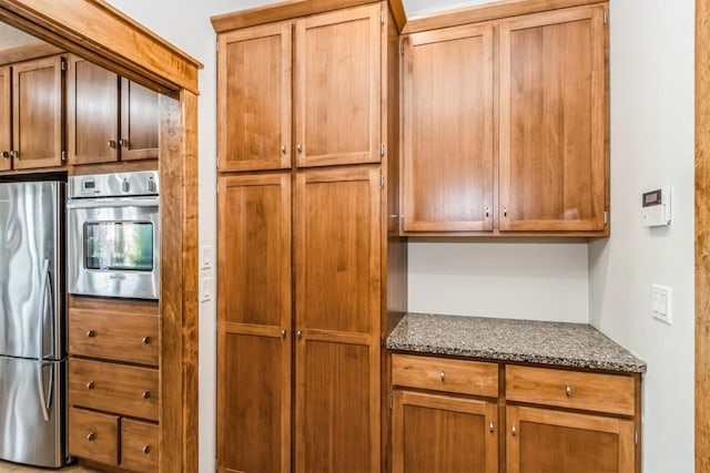 kitchen featuring dark stone countertops, brown cabinetry, and stainless steel appliances