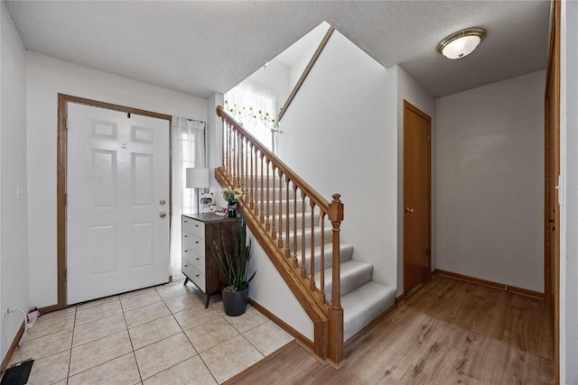 entryway with light tile patterned floors, stairway, a textured ceiling, and baseboards