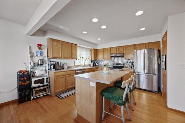 kitchen featuring a kitchen island, light wood-style flooring, stainless steel appliances, light countertops, and a kitchen bar