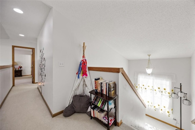 hall featuring baseboards, light carpet, a textured ceiling, and an upstairs landing