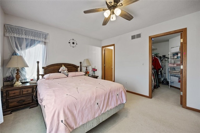 bedroom featuring visible vents, a walk in closet, a closet, baseboards, and light colored carpet