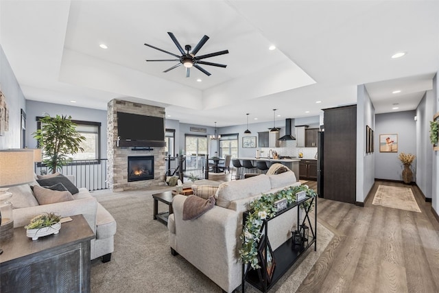 living area with baseboards, recessed lighting, a fireplace, ceiling fan, and a raised ceiling