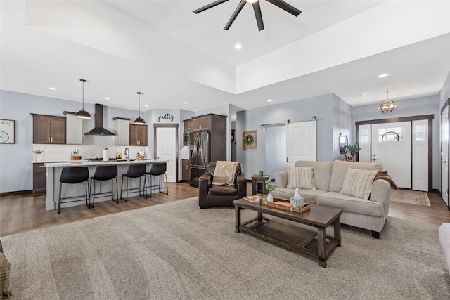 living area with a ceiling fan, wood finished floors, recessed lighting, a barn door, and baseboards