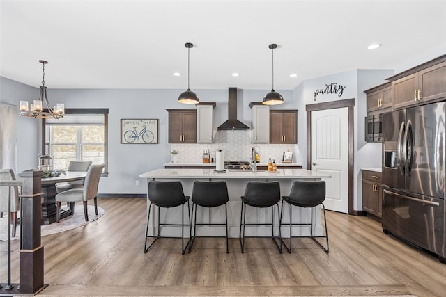 kitchen featuring backsplash, wall chimney range hood, light countertops, a notable chandelier, and stainless steel appliances