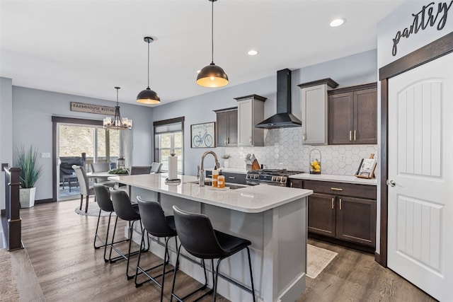 kitchen with stainless steel range with gas stovetop, a sink, light countertops, wall chimney exhaust hood, and tasteful backsplash