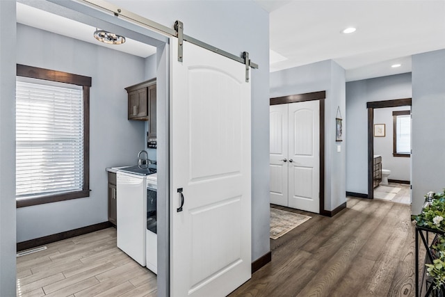 washroom featuring washing machine and clothes dryer, cabinet space, a sink, light wood-style floors, and a barn door