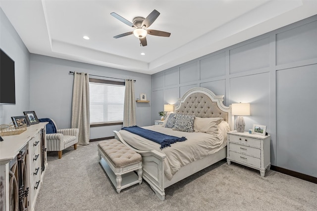 bedroom with recessed lighting, light carpet, a raised ceiling, and a decorative wall