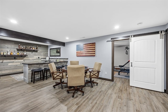 dining space featuring a barn door, a dry bar, baseboards, and light wood-type flooring