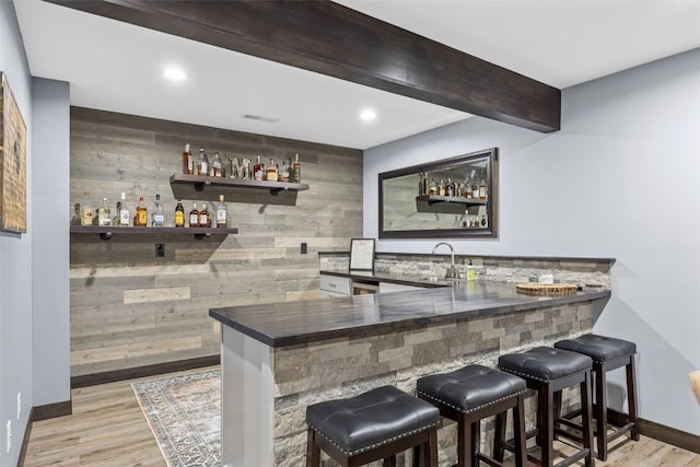 bar with indoor wet bar, wooden walls, and light wood-type flooring