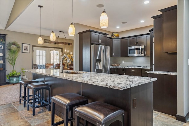 kitchen featuring dark brown cabinetry, light stone counters, stone finish floor, stainless steel appliances, and a sink