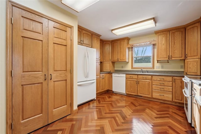 kitchen featuring white appliances, dark countertops, and a sink