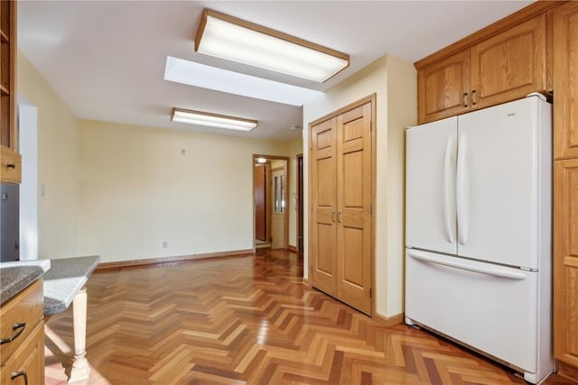 kitchen with brown cabinets, stone countertops, freestanding refrigerator, and baseboards