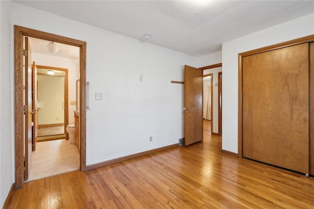 unfurnished bedroom with ensuite bath, baseboards, light wood-type flooring, and a closet