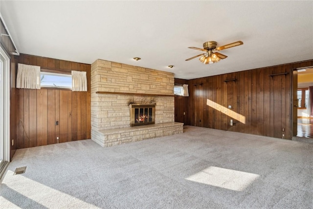 unfurnished living room featuring wooden walls, visible vents, carpet flooring, a fireplace, and a ceiling fan