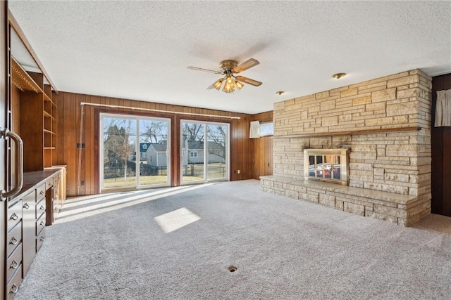 unfurnished living room featuring carpet floors, a stone fireplace, wood walls, and a ceiling fan