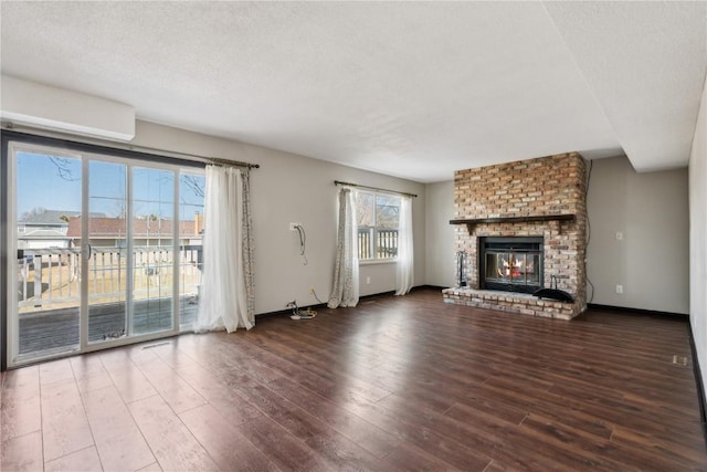 unfurnished living room featuring a brick fireplace, a textured ceiling, baseboards, and wood finished floors