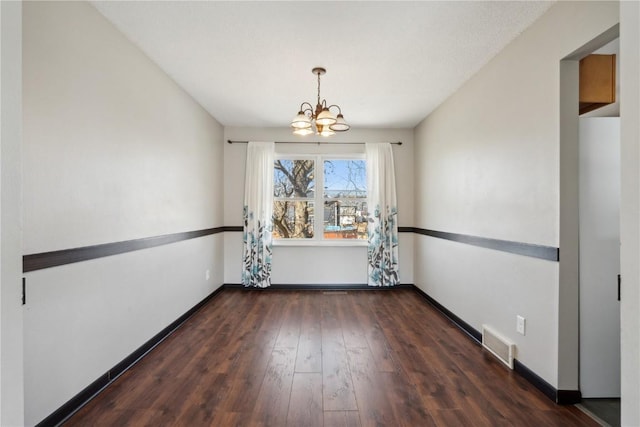 unfurnished dining area with visible vents, wood-type flooring, a notable chandelier, and baseboards