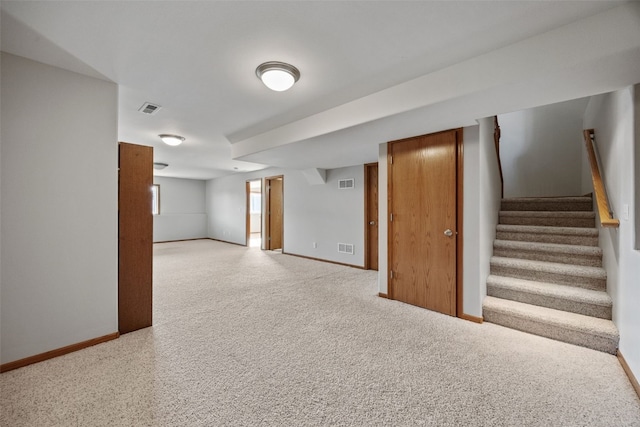 finished below grade area featuring visible vents, baseboards, light colored carpet, and stairs